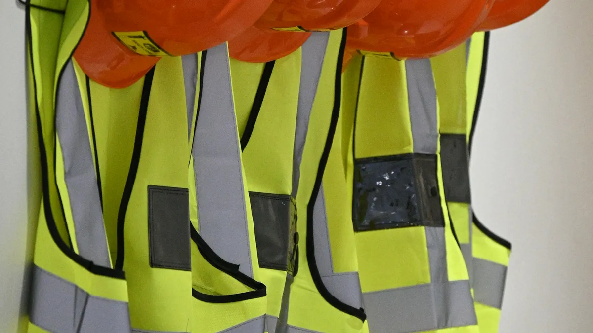 Orange hard hats and high-visibility safety vests hanging on a wall
