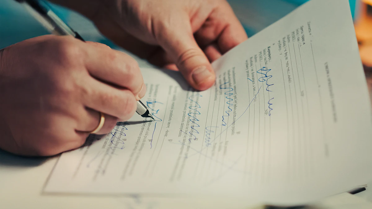 Close-up of a hand signing a printed multi-page document with a pen